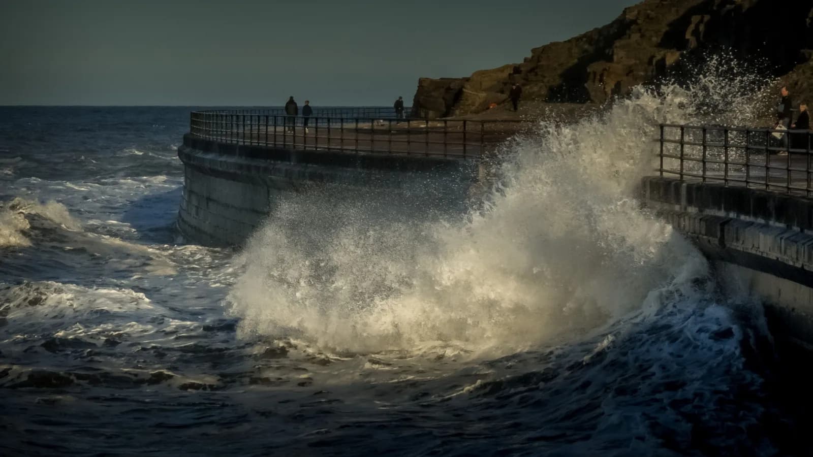 Powerful ocean waves crashing against a seawall with a dramatic background.