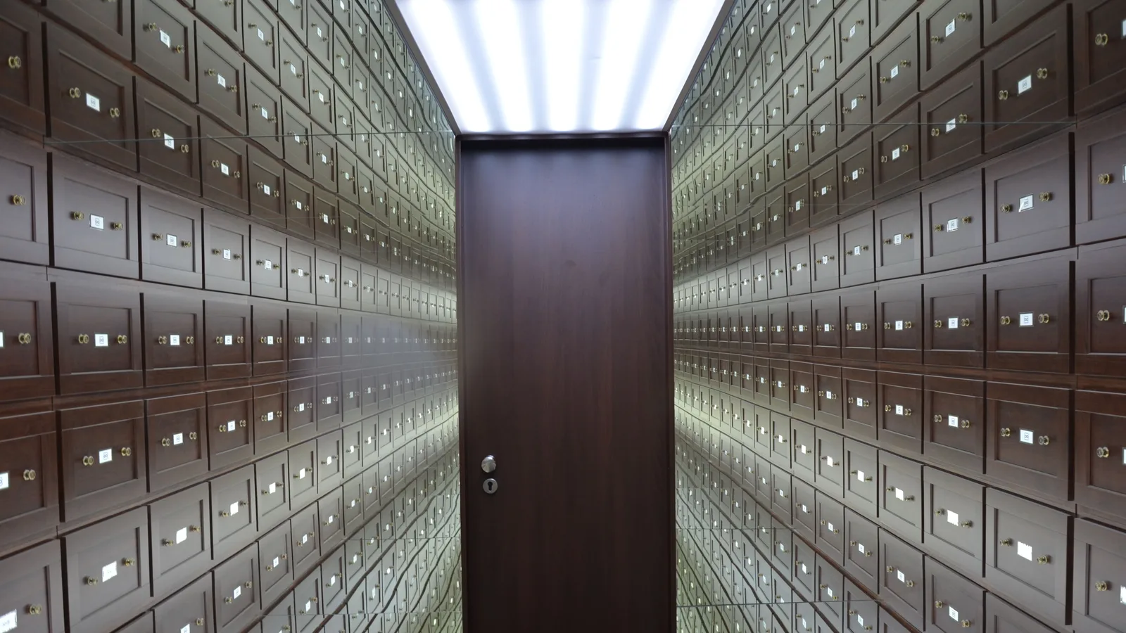 Wooden lockboxes line the walls of a modern, secure vault with a central wooden door.