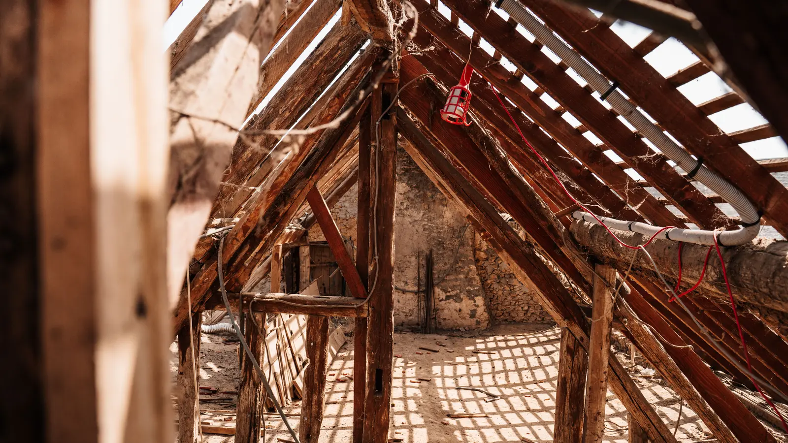 Interior view of wooden framing and rafters in a partially constructed attic space, highlighting a rustic and textured structure.
