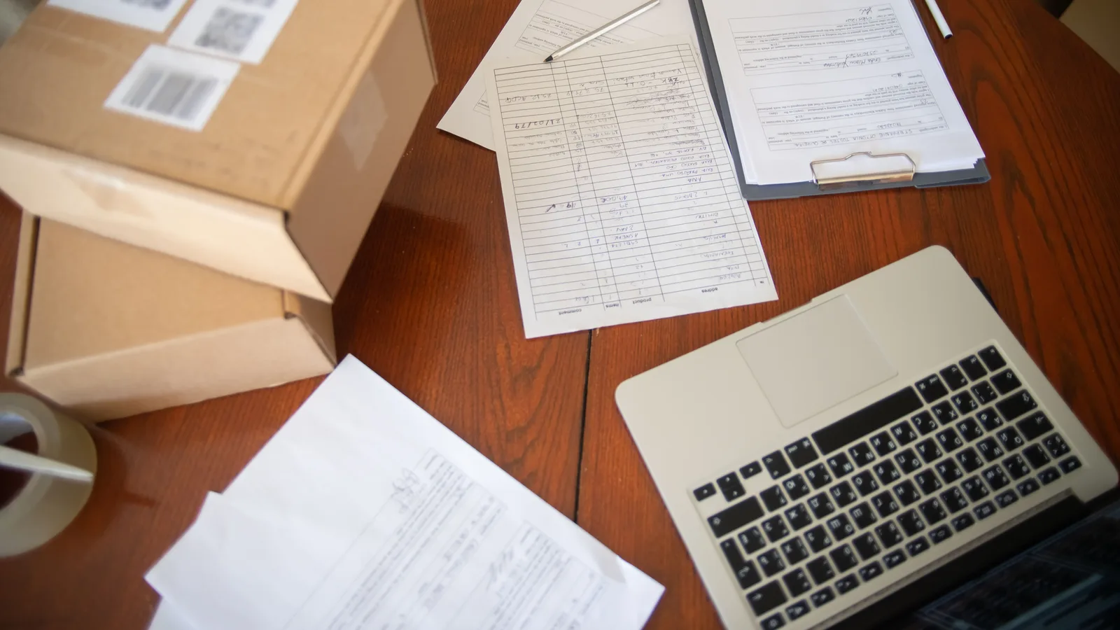 Flat lay of a workspace with laptop, documents, and cardboard boxes for e-commerce operations.