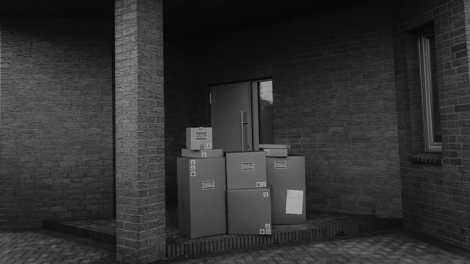 Grayscale photo showing stacked parcels by a building's doorway, evoking modern delivery themes.