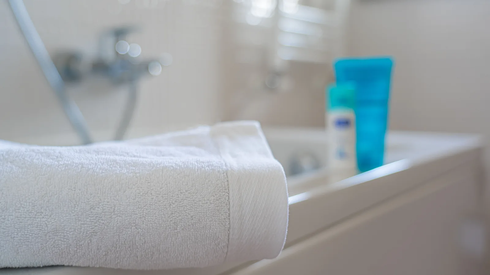 Folded white towel draped over a bathtub rim with toiletries in the background