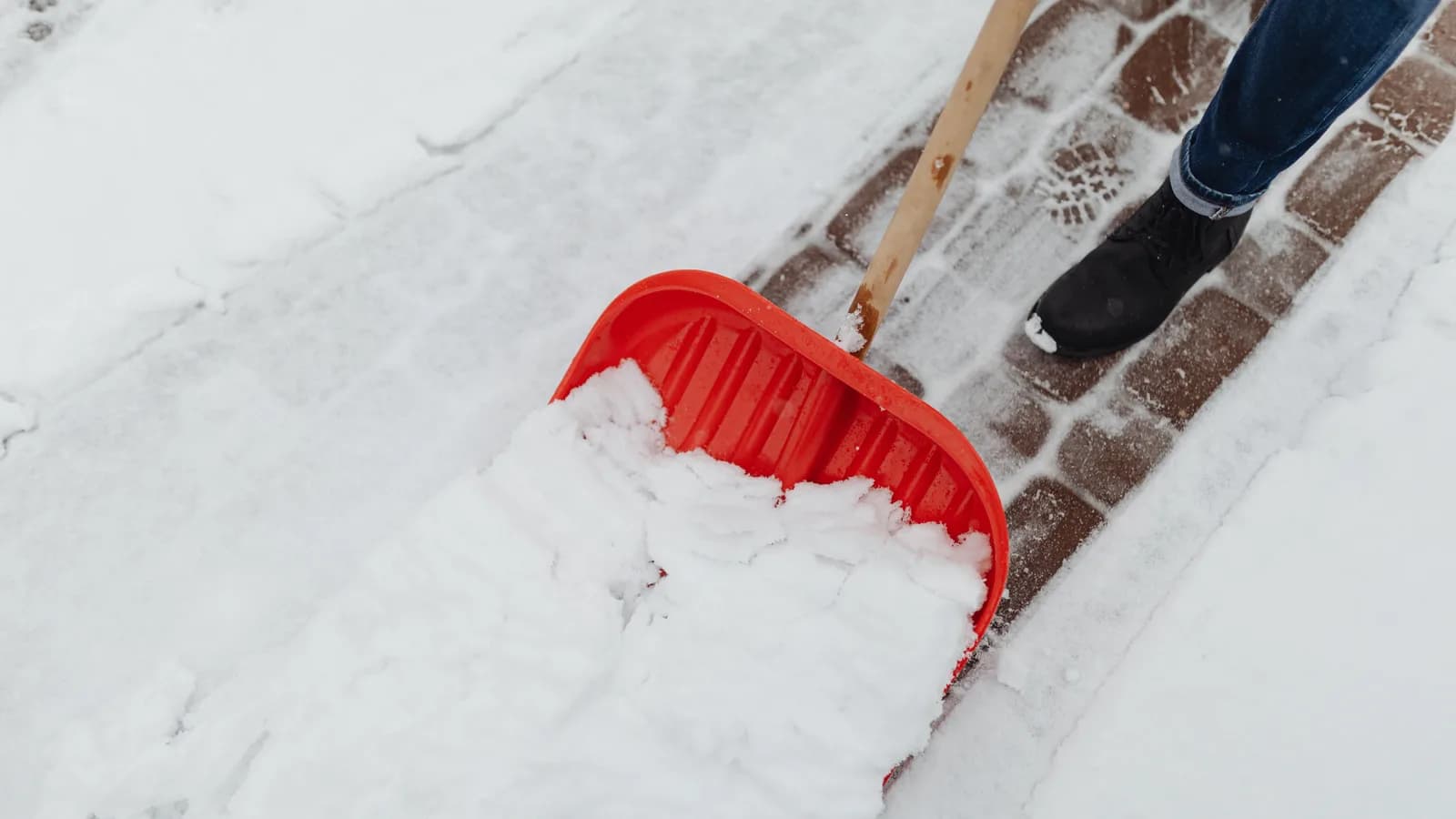 Person pushing snow from a brick walkway with a wide red shovel