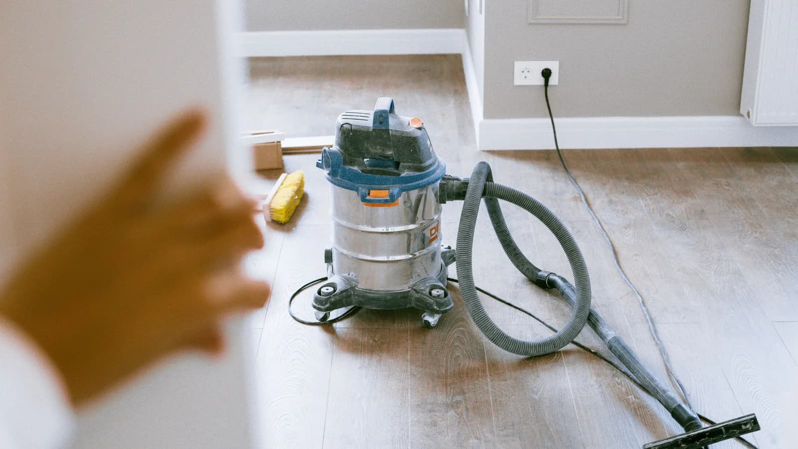 A wet/dry shop vacuum staged on a floor with its hose and attachments nearby.