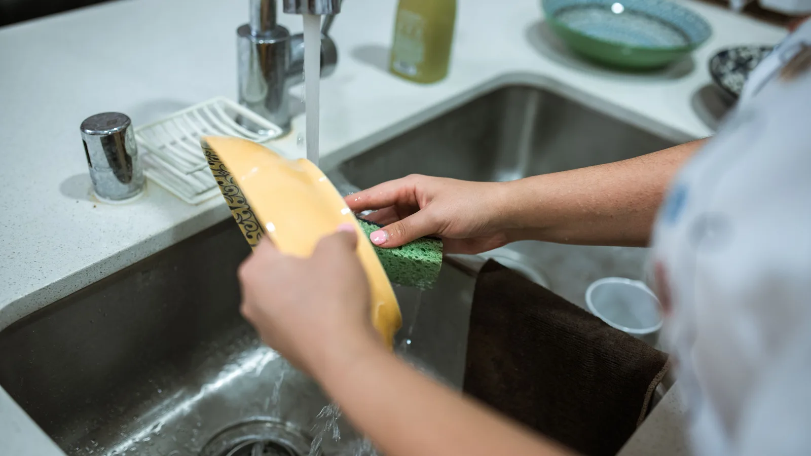 Hands rinsing a kitchen item under running water at the sink