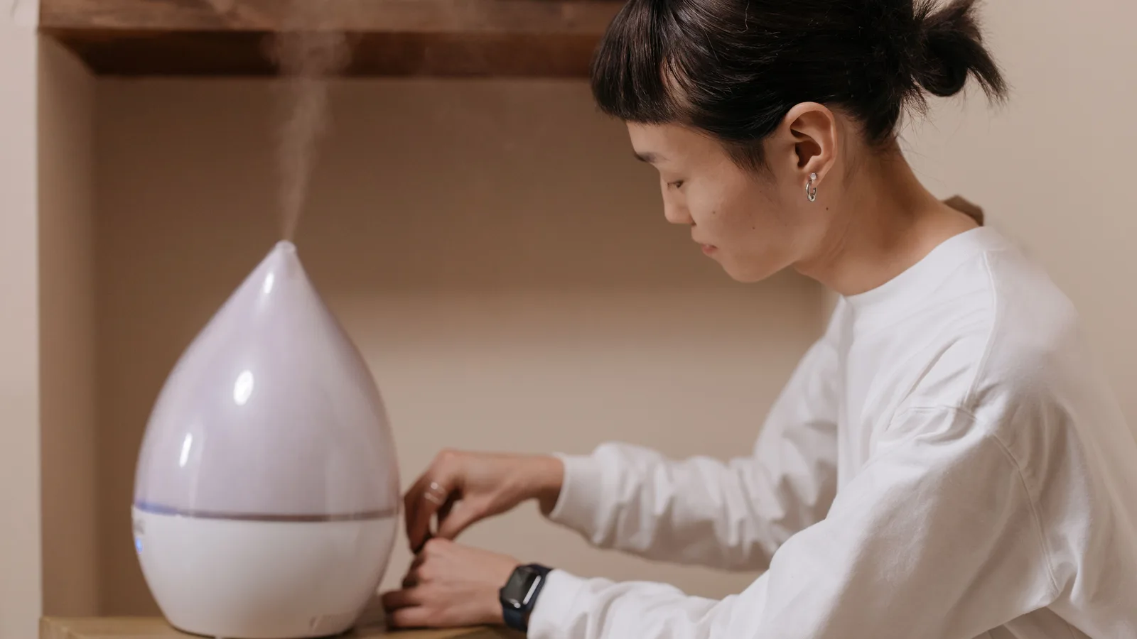 Person adjusting a teardrop-shaped portable humidifier on a wooden table