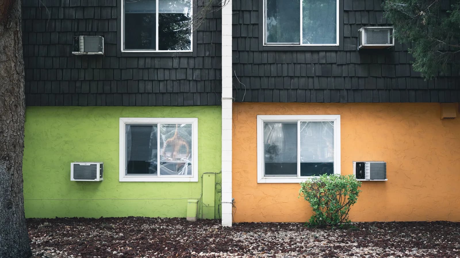 Four window air conditioners mounted on the exterior walls of a two-story apartment building