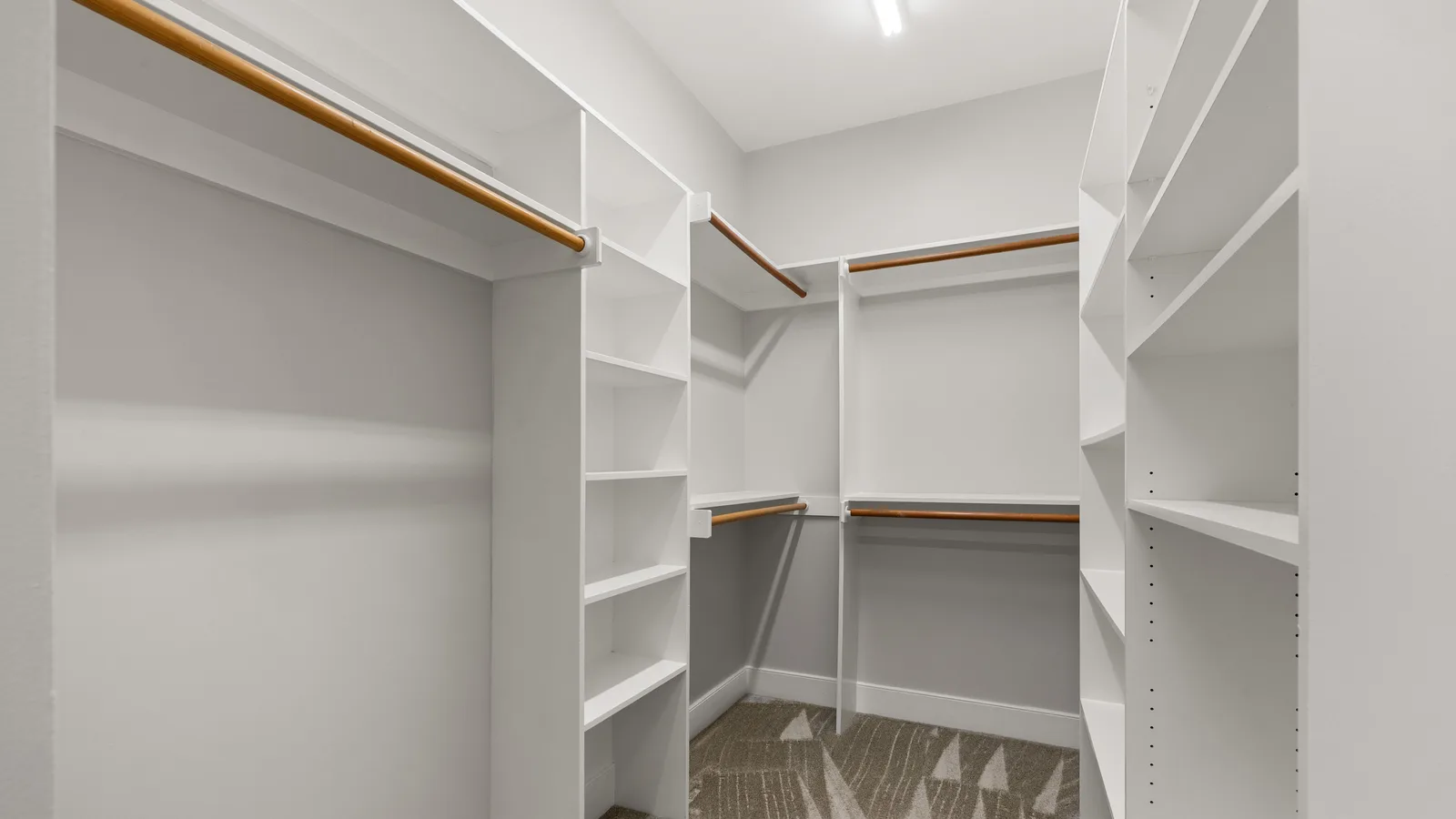 Modern empty walk-in closet with white shelving and brown rods, ready for organization.