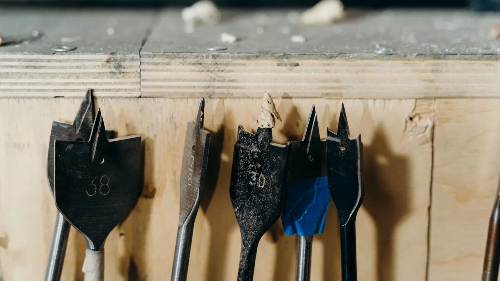 Detailed view of woodworking drill bits on a wooden surface in a workshop environment.