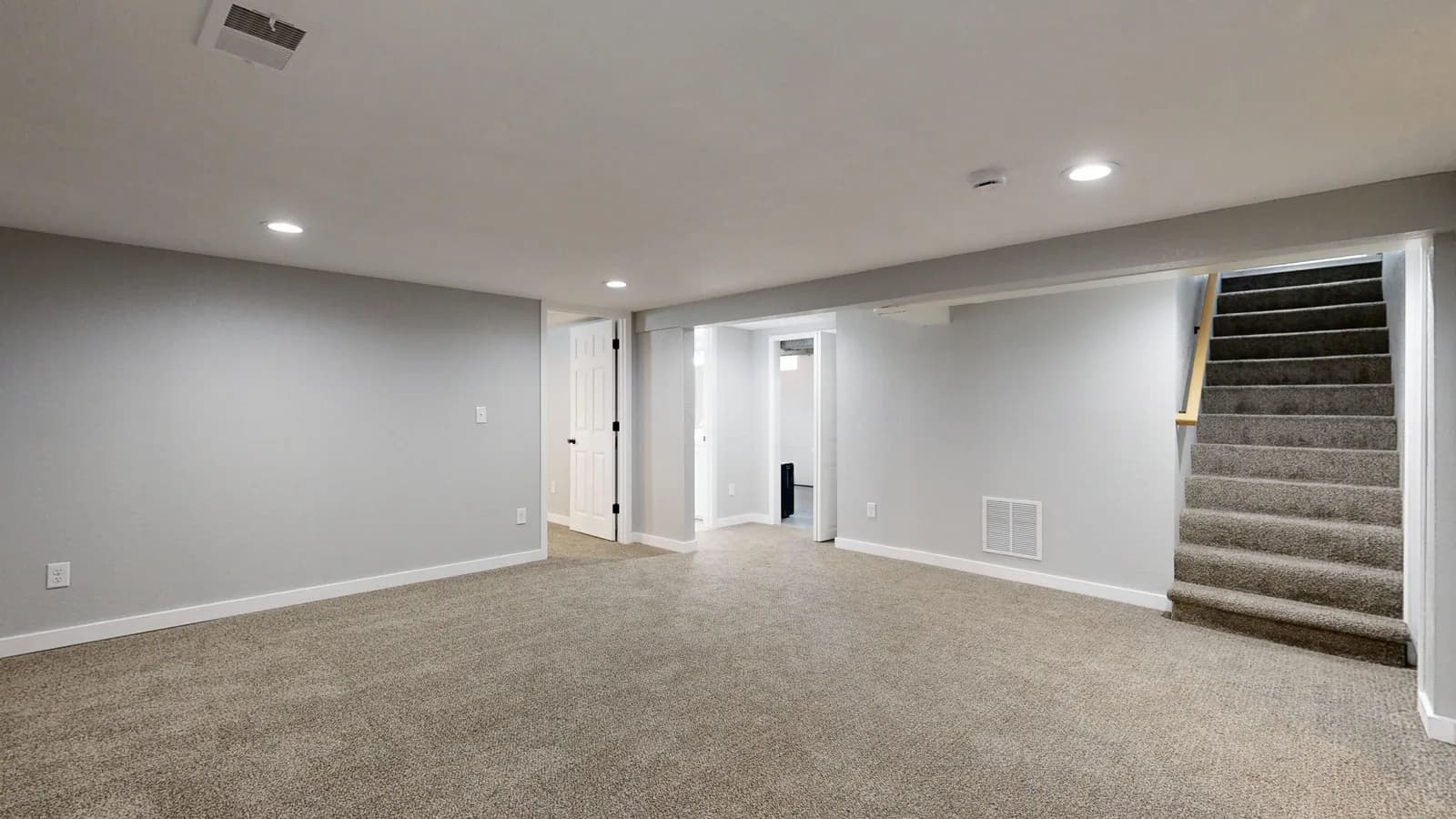 Empty modern basement with beige carpet and white walls, ideal for renovation.