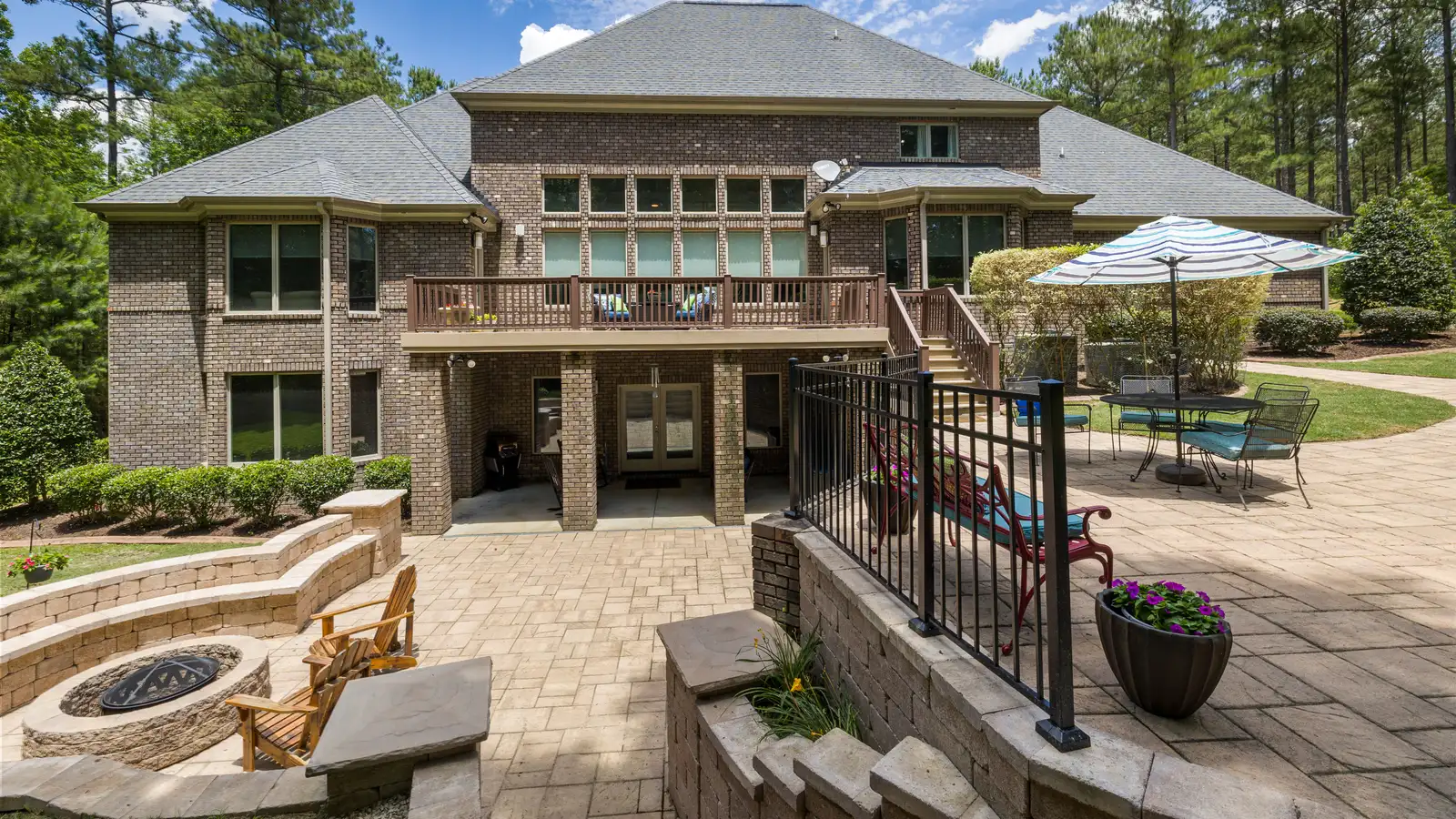 Large brick house with a stone terrace, fire pit, and well-maintained backyard garden.