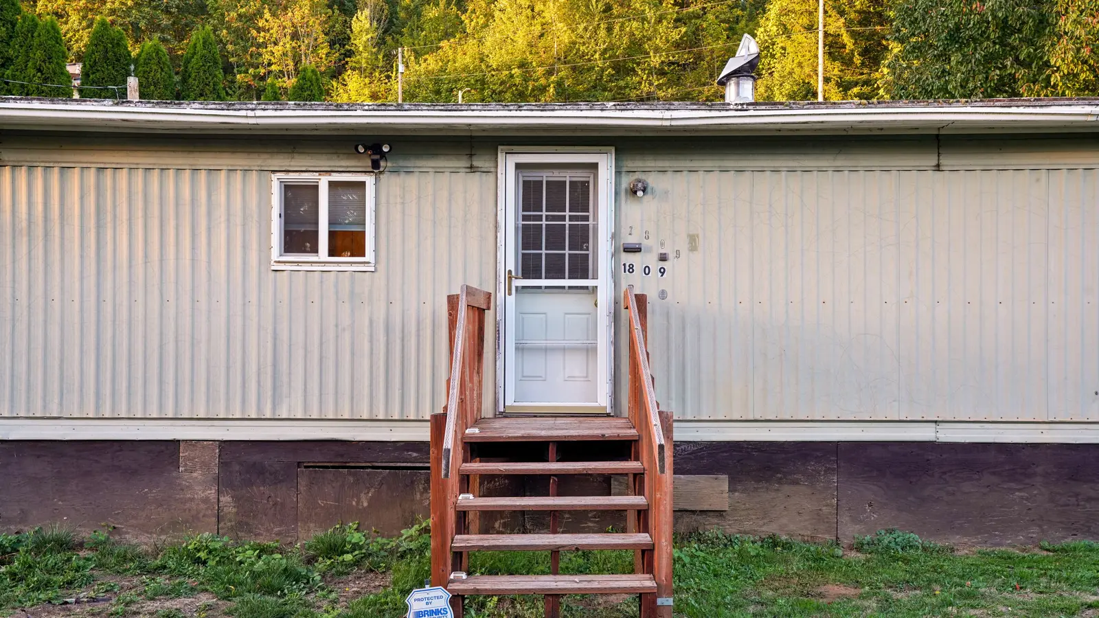 Exterior view of a mobile home with wooden steps on a sunny day.