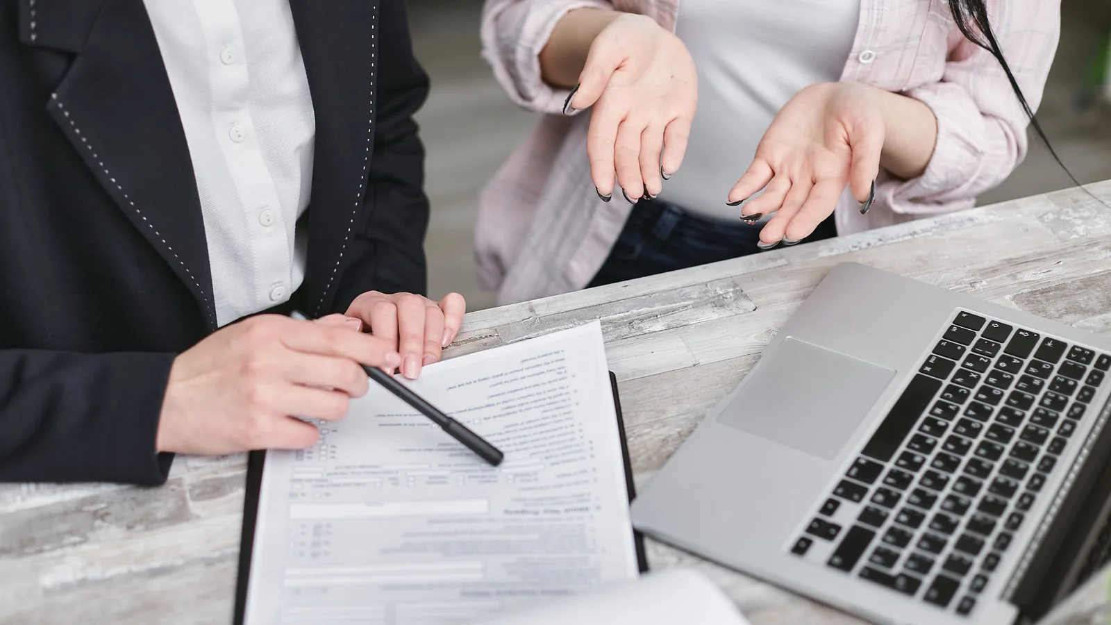 Two professionals discussing a contract at a business meeting with documents and a laptop.