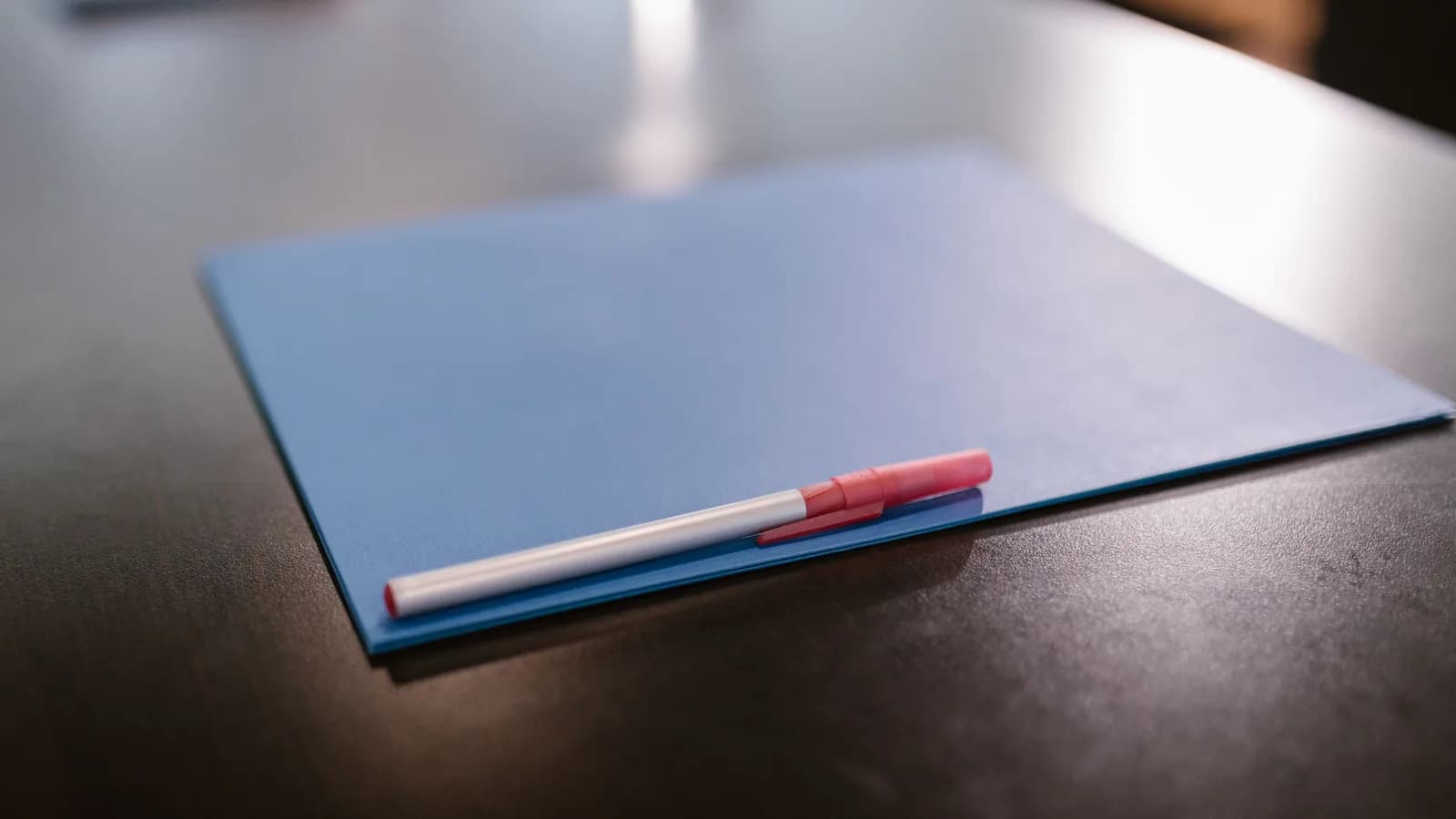 Close-up of a blue folder and pen on a table in a modern office environment.