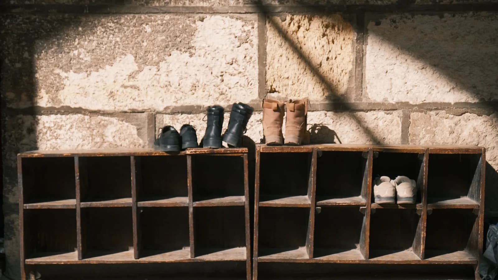 Wooden entryway cubbies holding shoes and boots against a stone wall