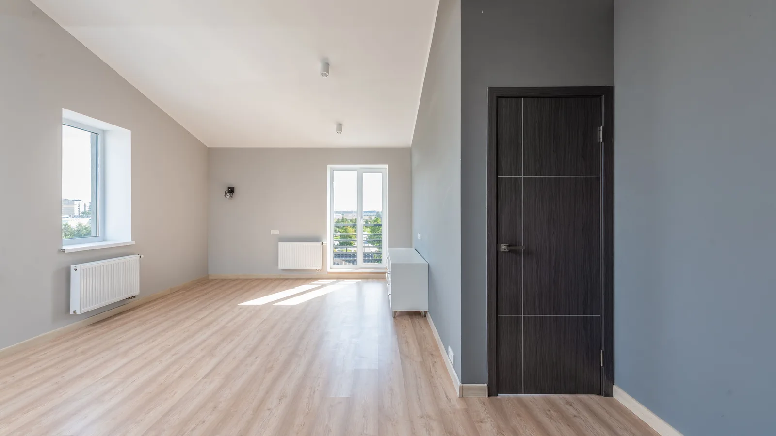 White radiators below windows in an unfurnished room with a clear wood floor path