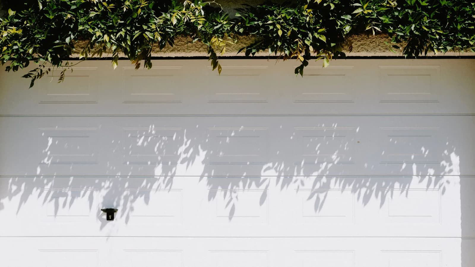 Closed white sectional garage door with the rigid lower section visible below the horizontal joint