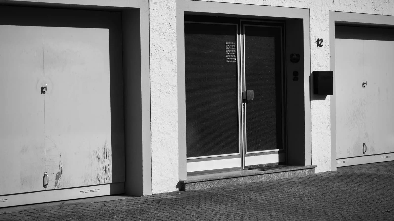 Monochrome photo of an urban building facade with garages and doors.