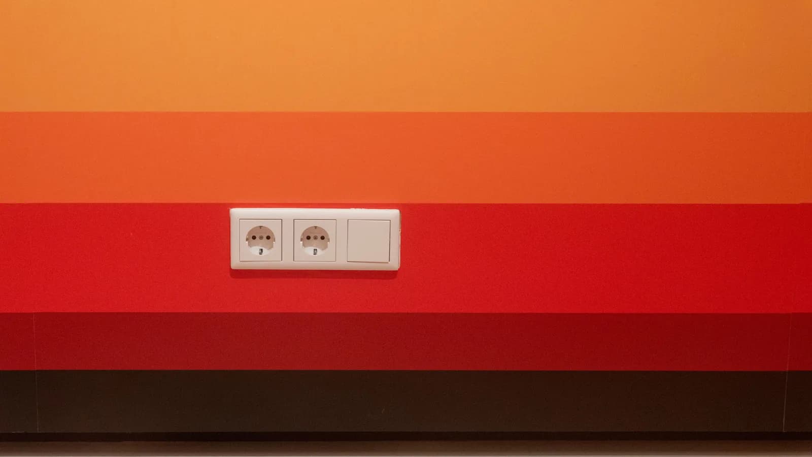 Minimalist design of orange and red striped wall with dual sockets.