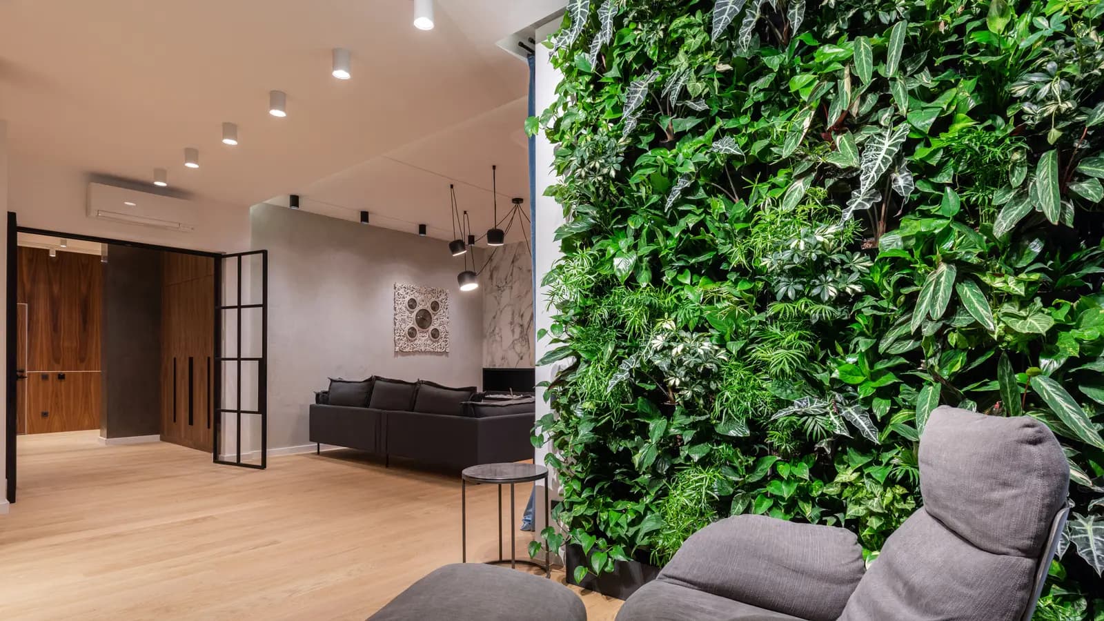 Interior of light modern flat with armchair with pouf near green wall with plants leaves