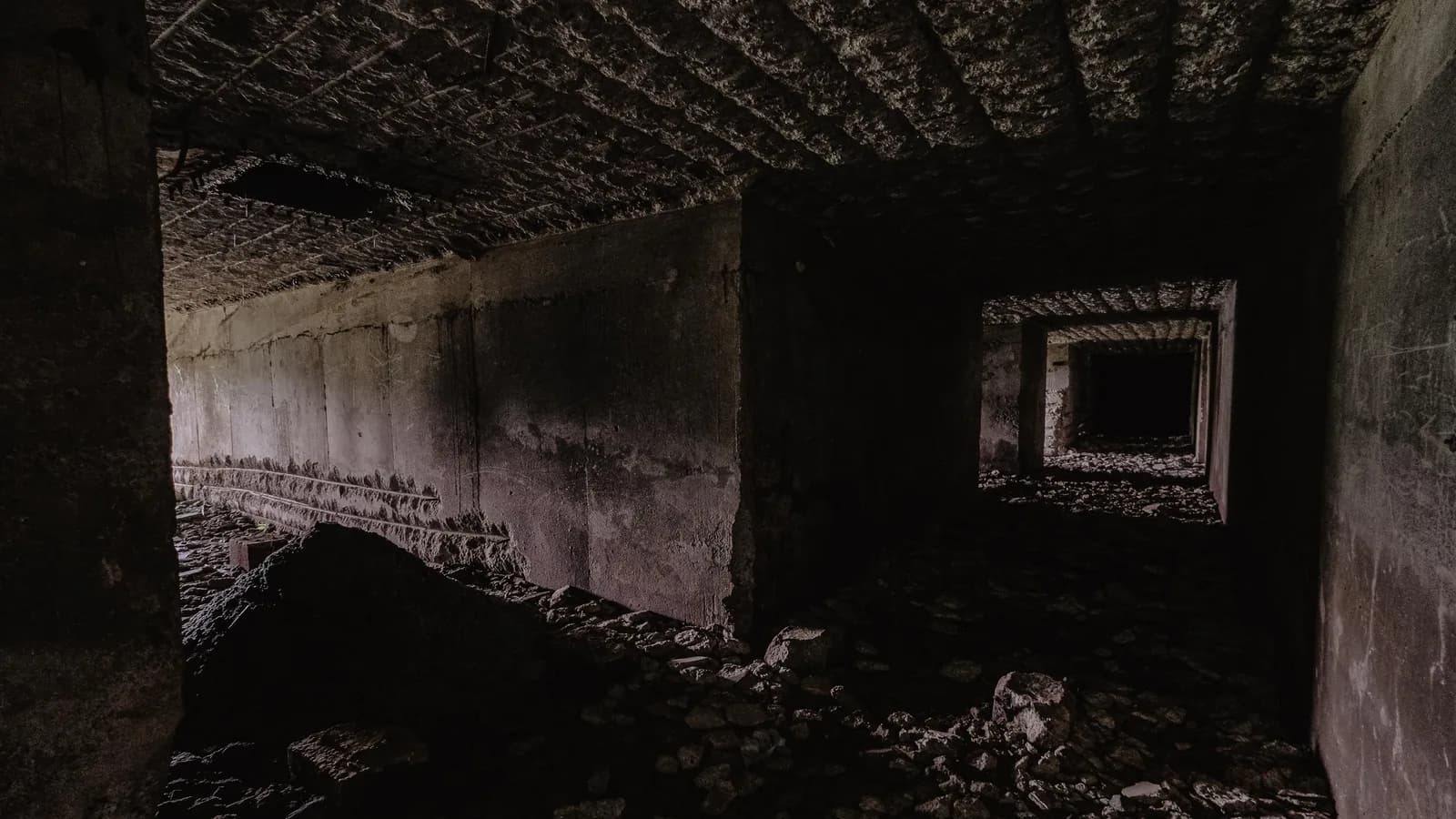 Dark, eerie underground hallway with scattered rocks and unfinished concrete surfaces.