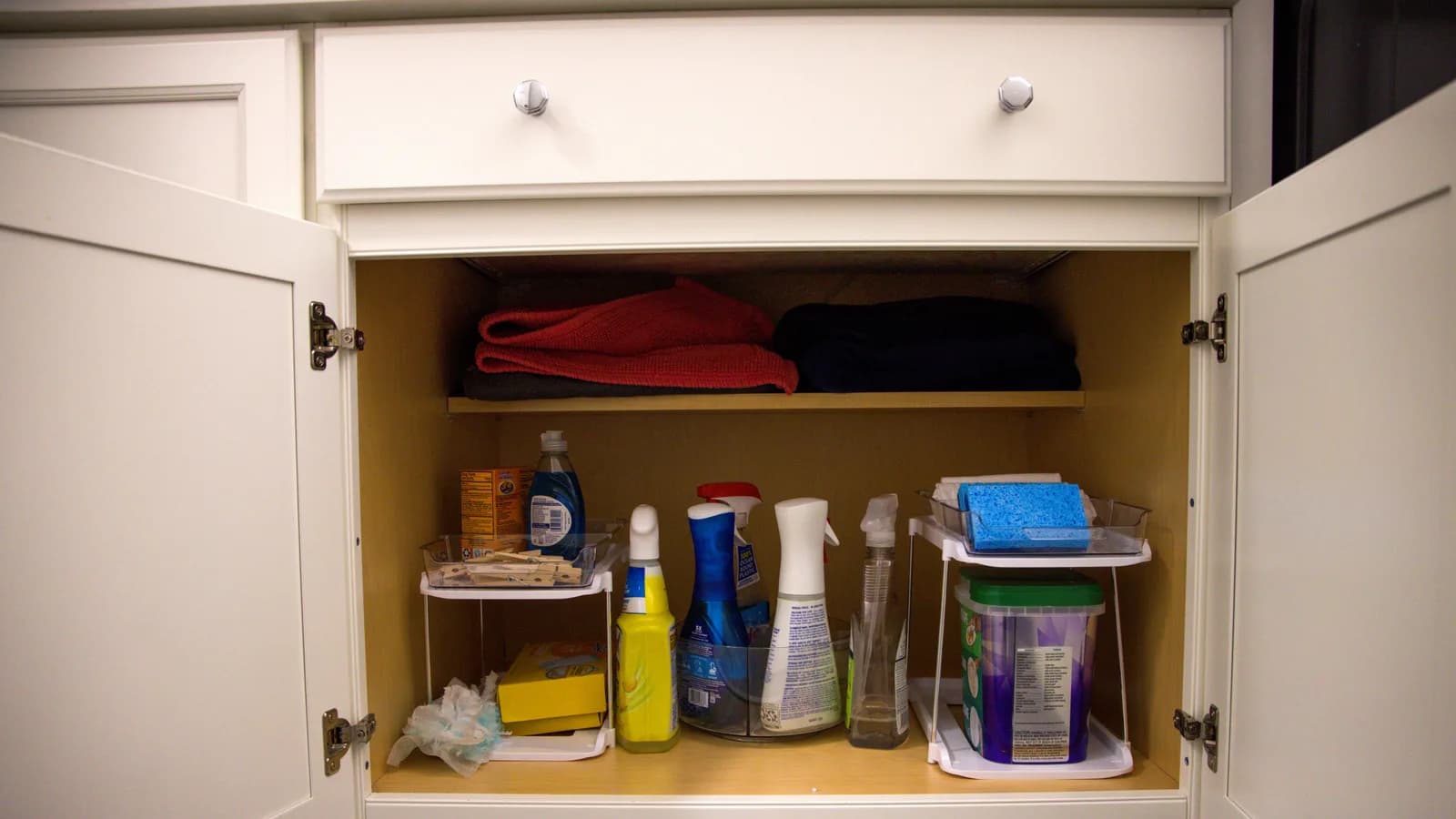 Cleaning bottles, sponges, cloths, and caddies arranged in an open cabinet
