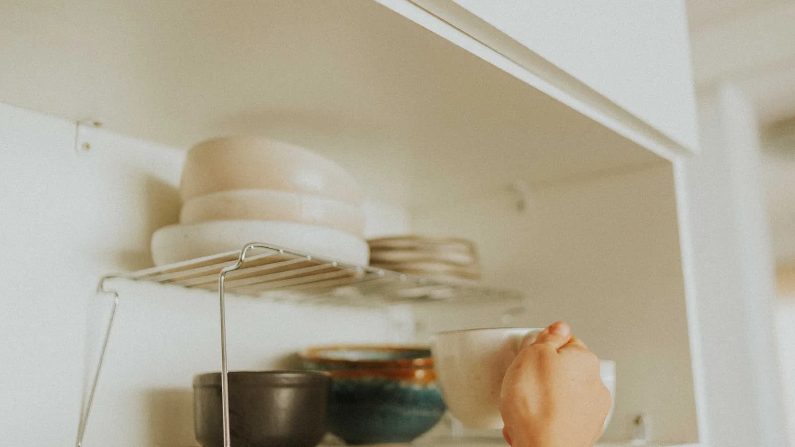 An open kitchen cabinet with bowls and cups arranged on a removable shelf riser
