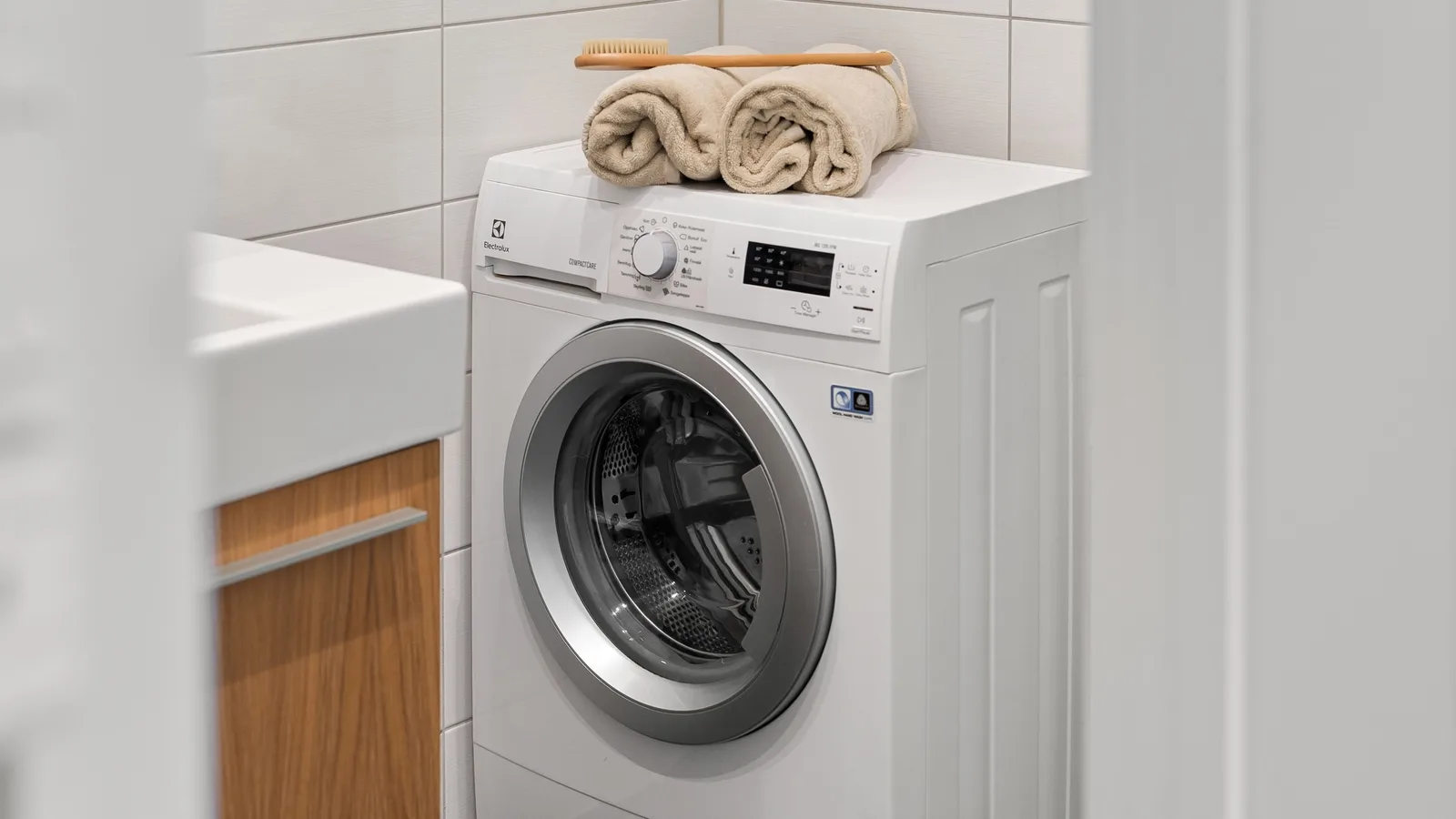 White front-loading washing machine beside a utility sink with folded towels on top
