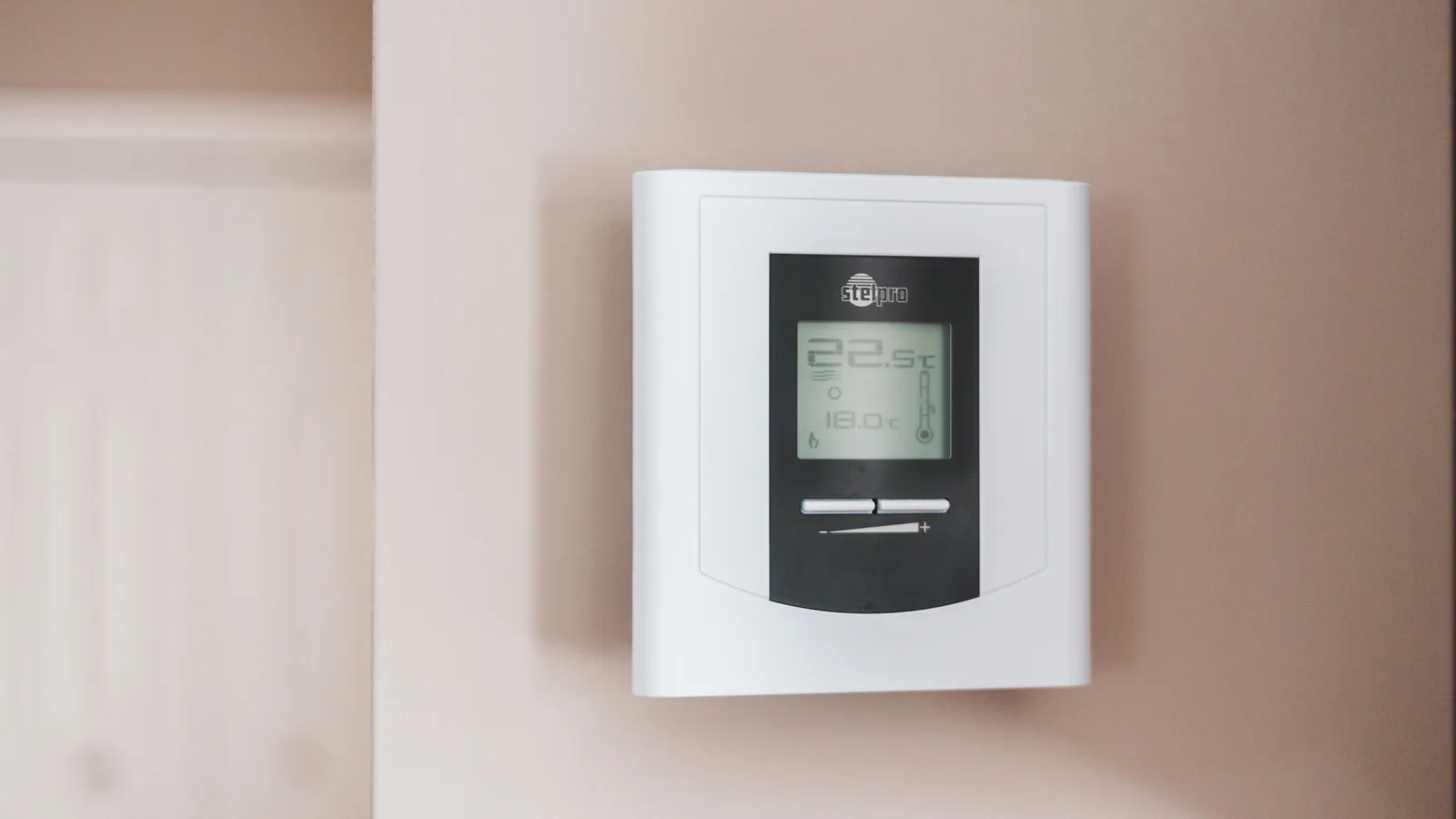 Close-up of a modern digital thermostat mounted on a wall, displaying temperature settings in Celsius.