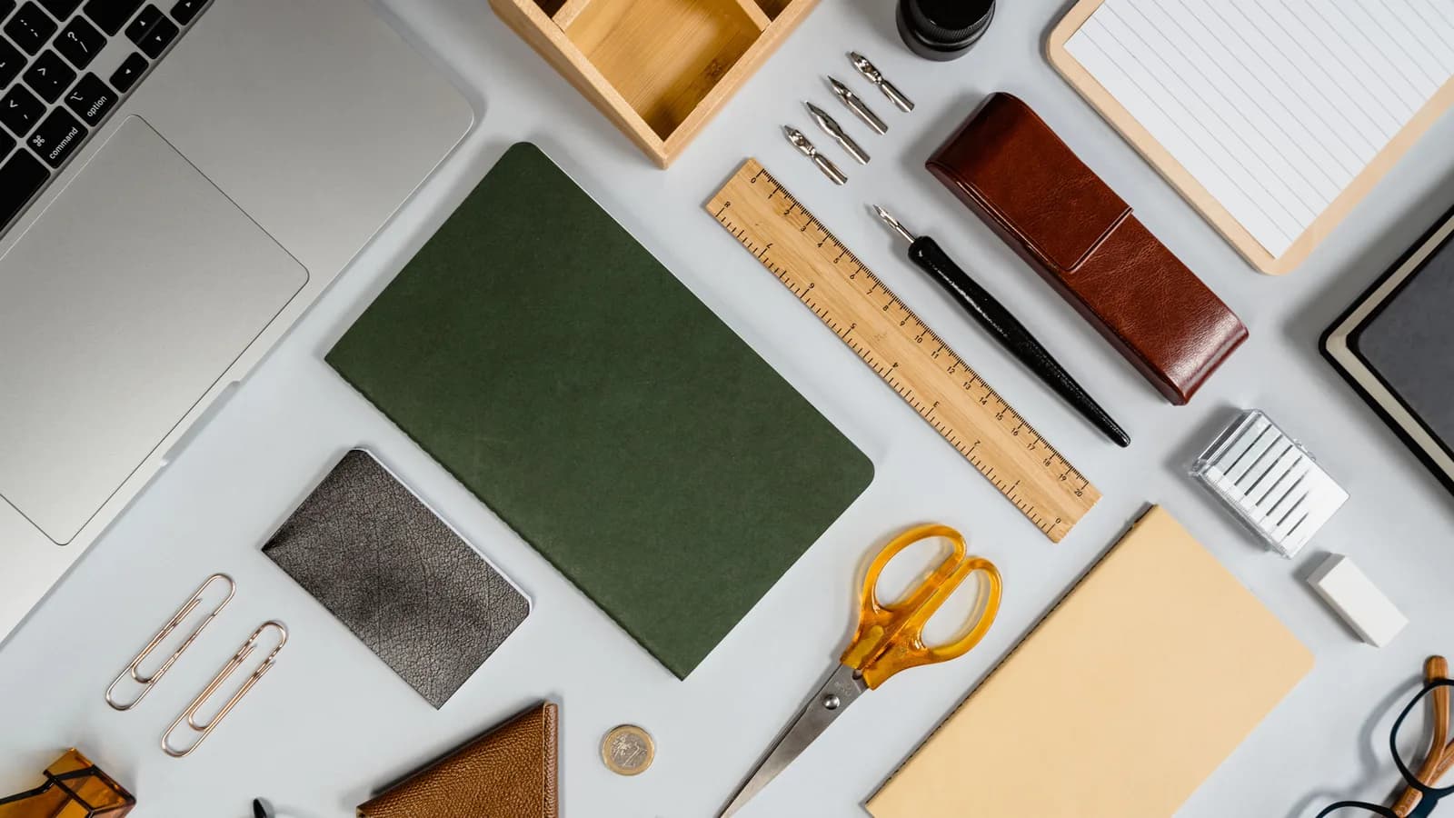 Organized flat lay of office supplies featuring a laptop, pens, scissors, and notebooks.
