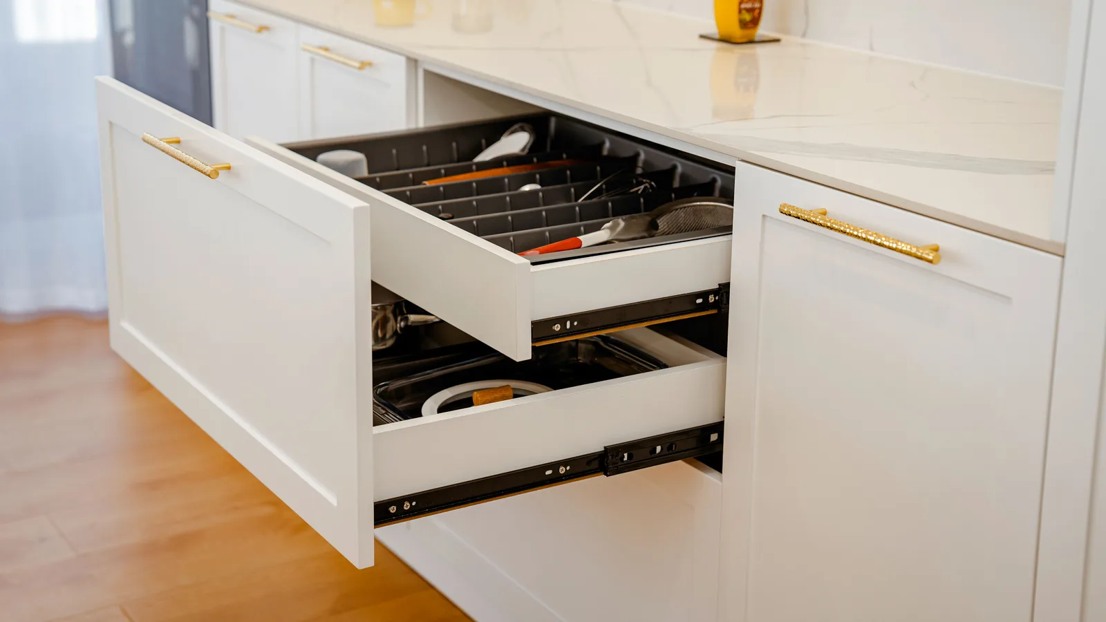 Elegant white kitchen drawer open with utensils, on marble counter.