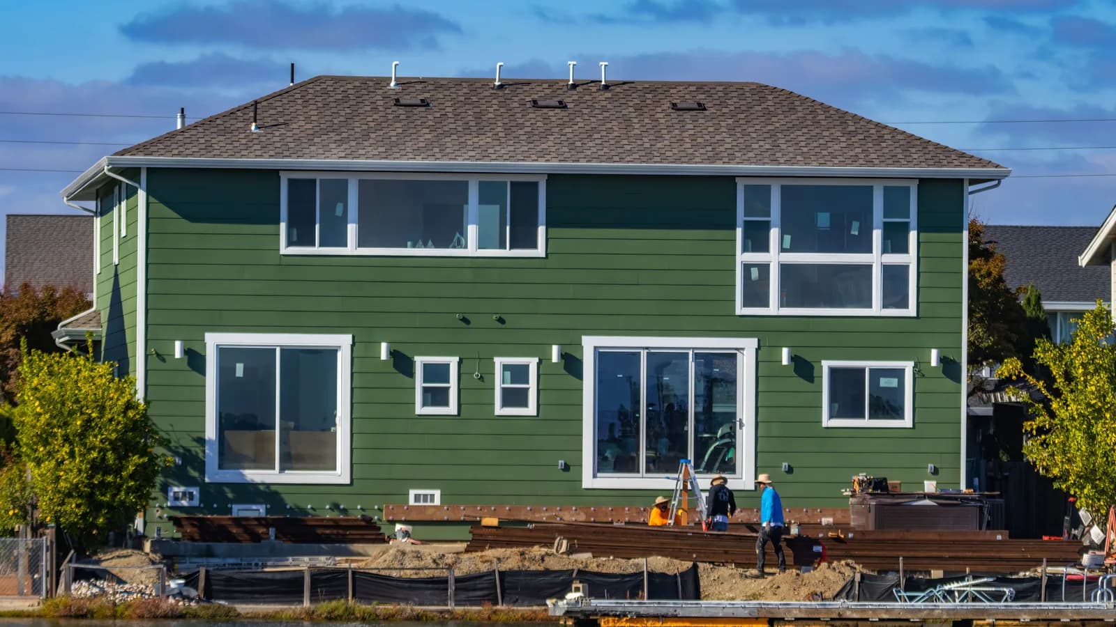 A modern green house under construction with blue skies and workers outside.