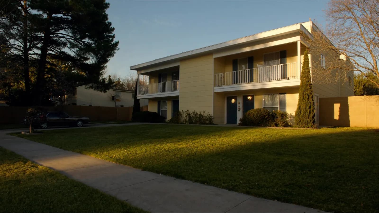 Two-story cream fourplex rental building with navy shutters and matching front doors, warm late-afternoon light on a quiet suburban street