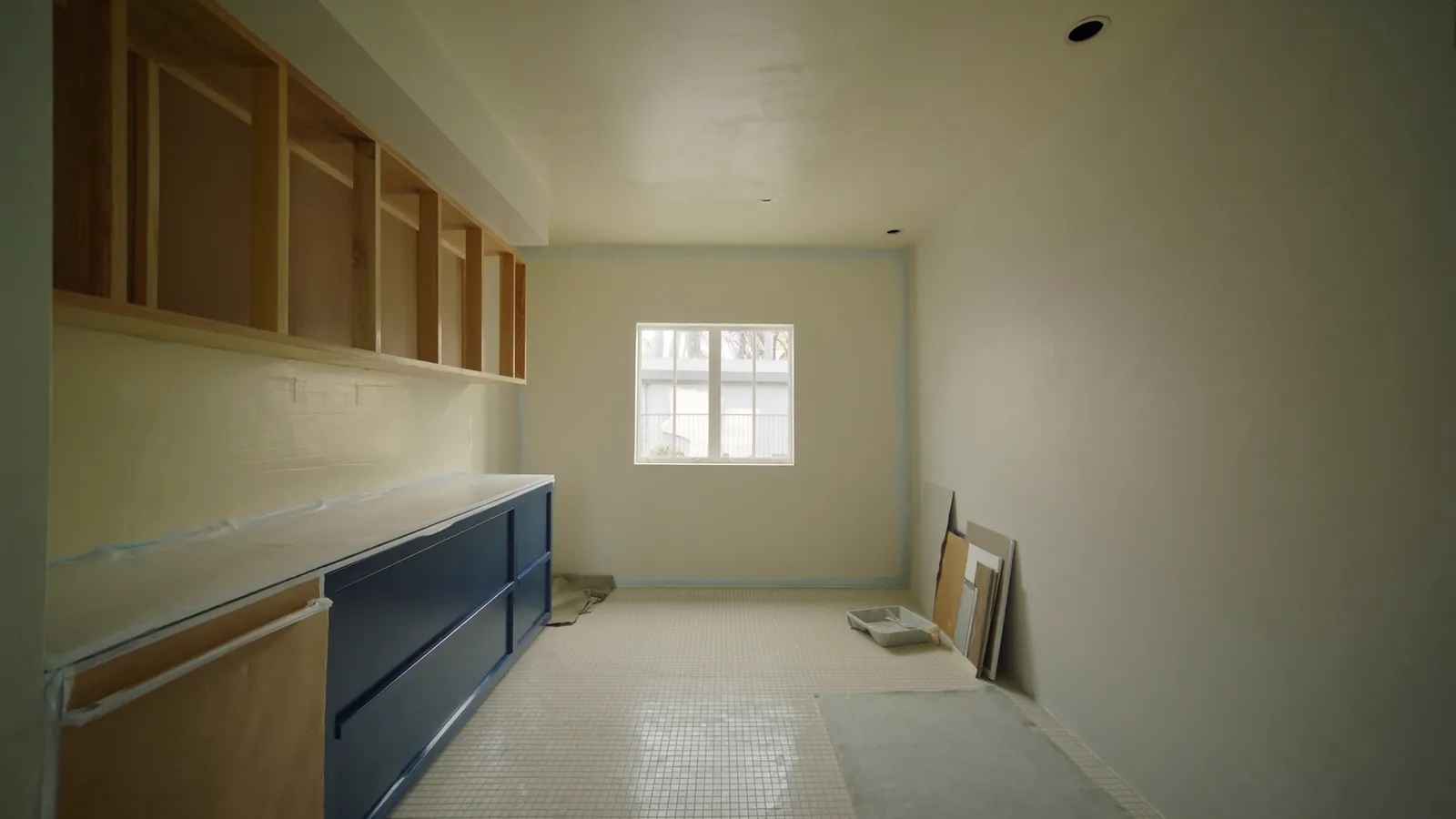 Tidy mid-renovation kitchen with new cabinet frames, navy cabinet accents, and organized supplies lit by soft daylight