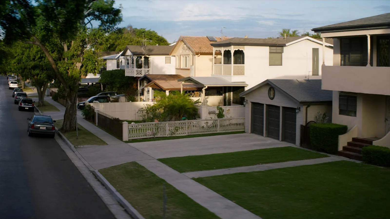 Suburban American street lined with varied single-family homes in cream, navy, and neutral tones under warm afternoon light