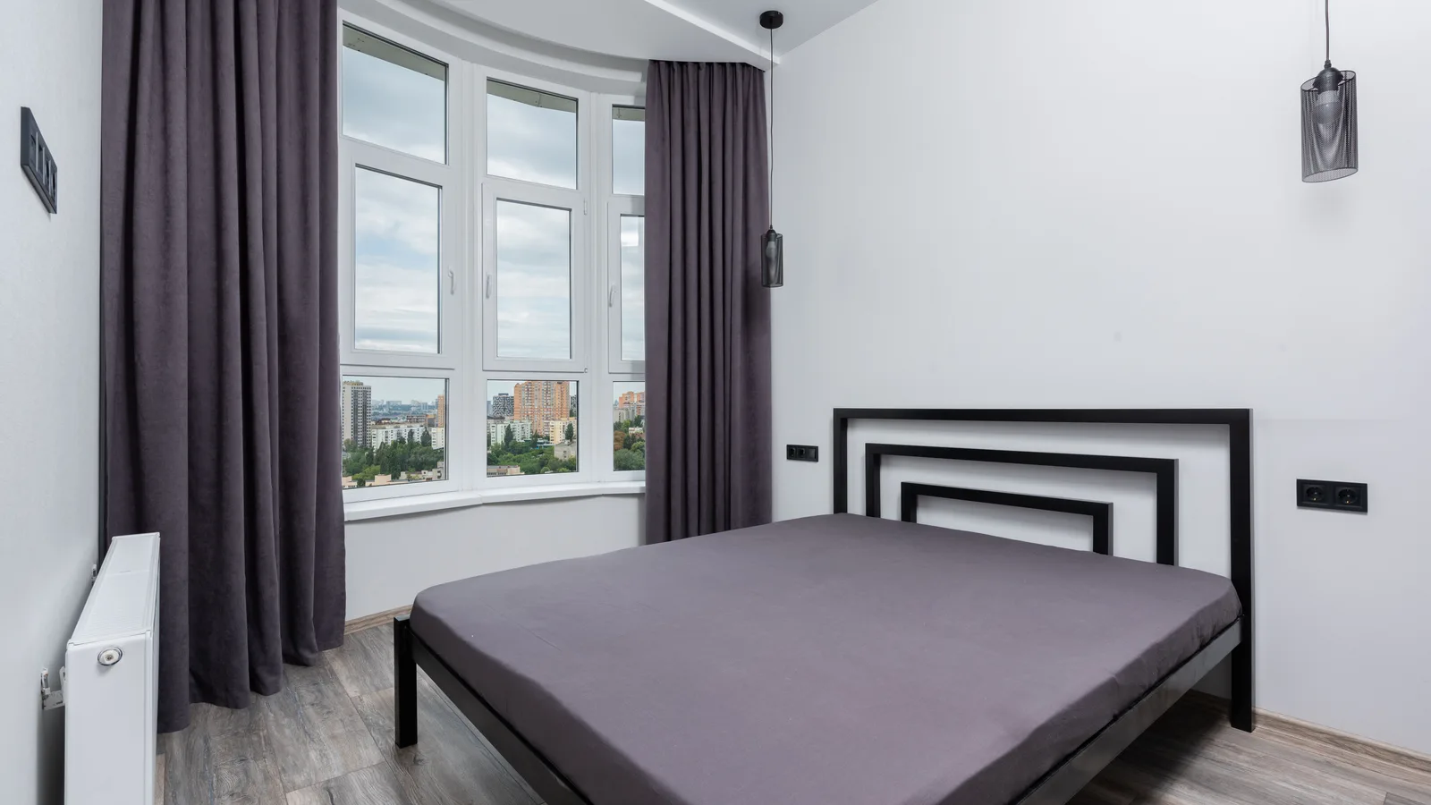 Dark floor-length curtain panels mounted beyond a wide bedroom window beside a bed