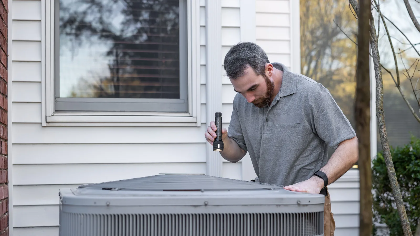 Technician inspecting a residential outdoor HVAC unit with a flashlight