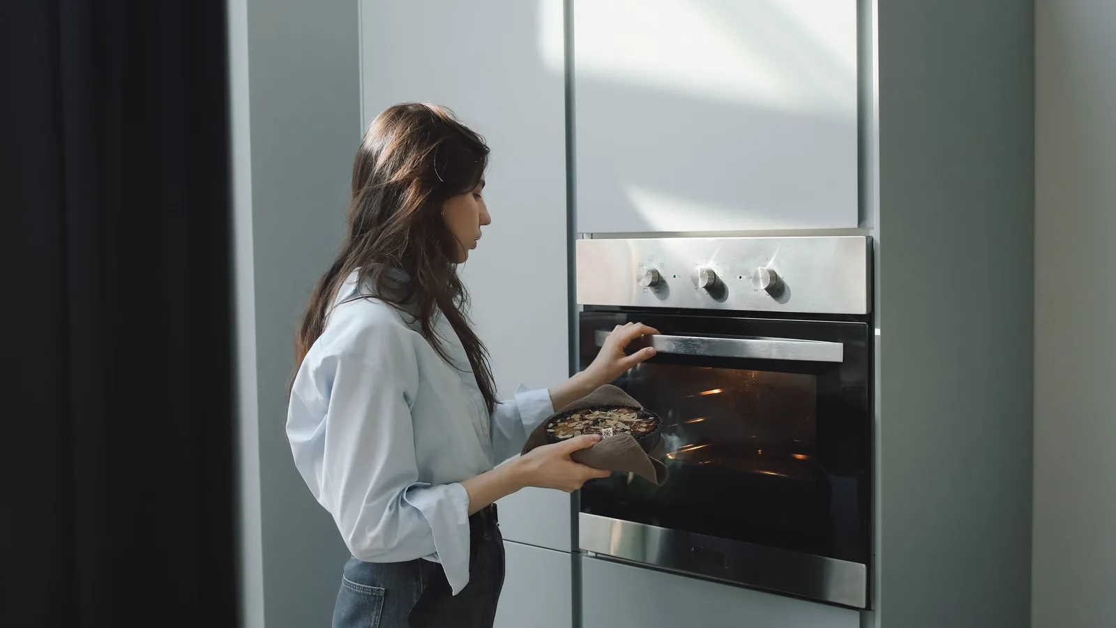 A home baker holding a tray beside a built-in oven with metal racks visible through the door