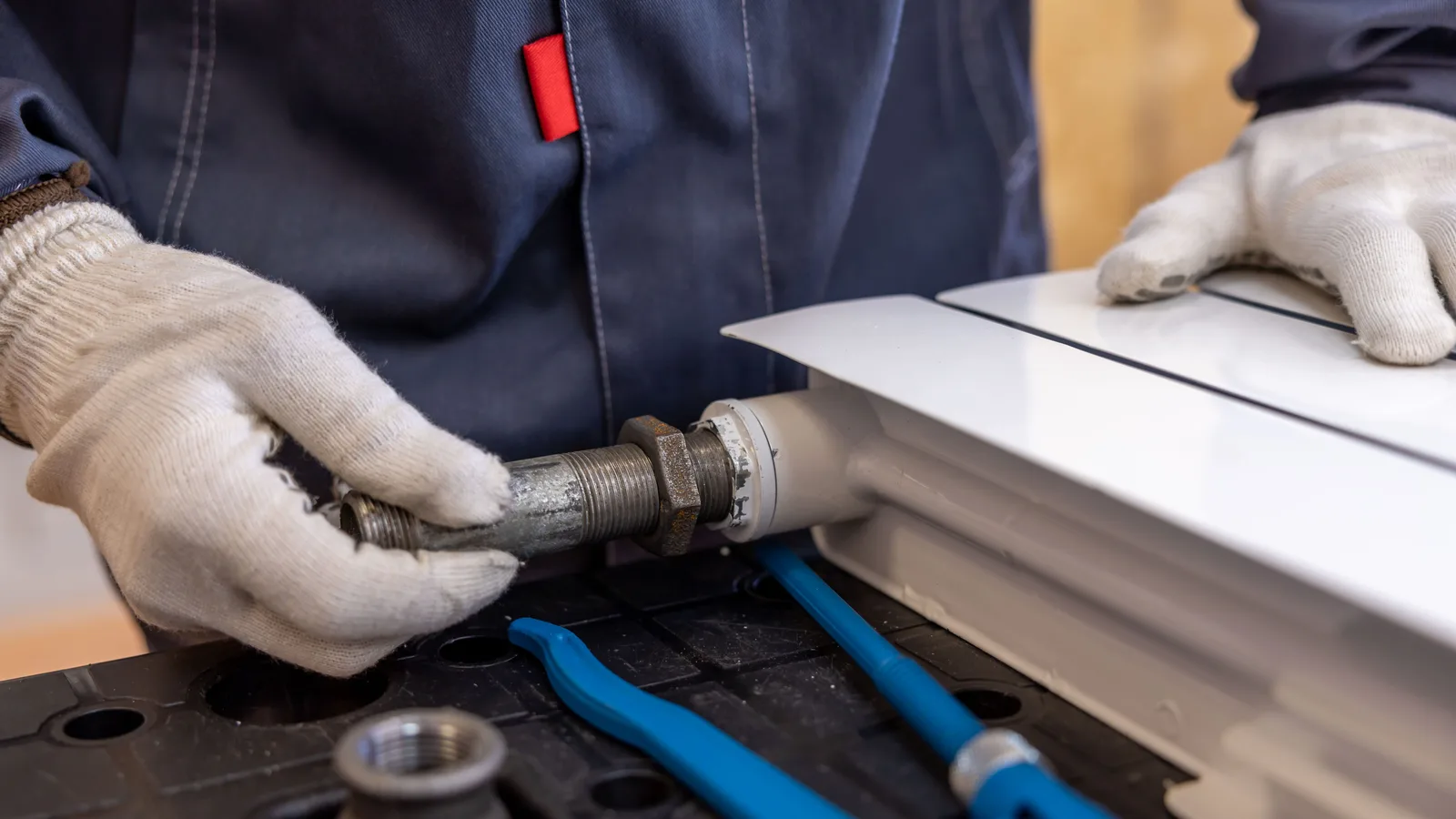 Gloved technician connecting a threaded metal pipe to a white radiator