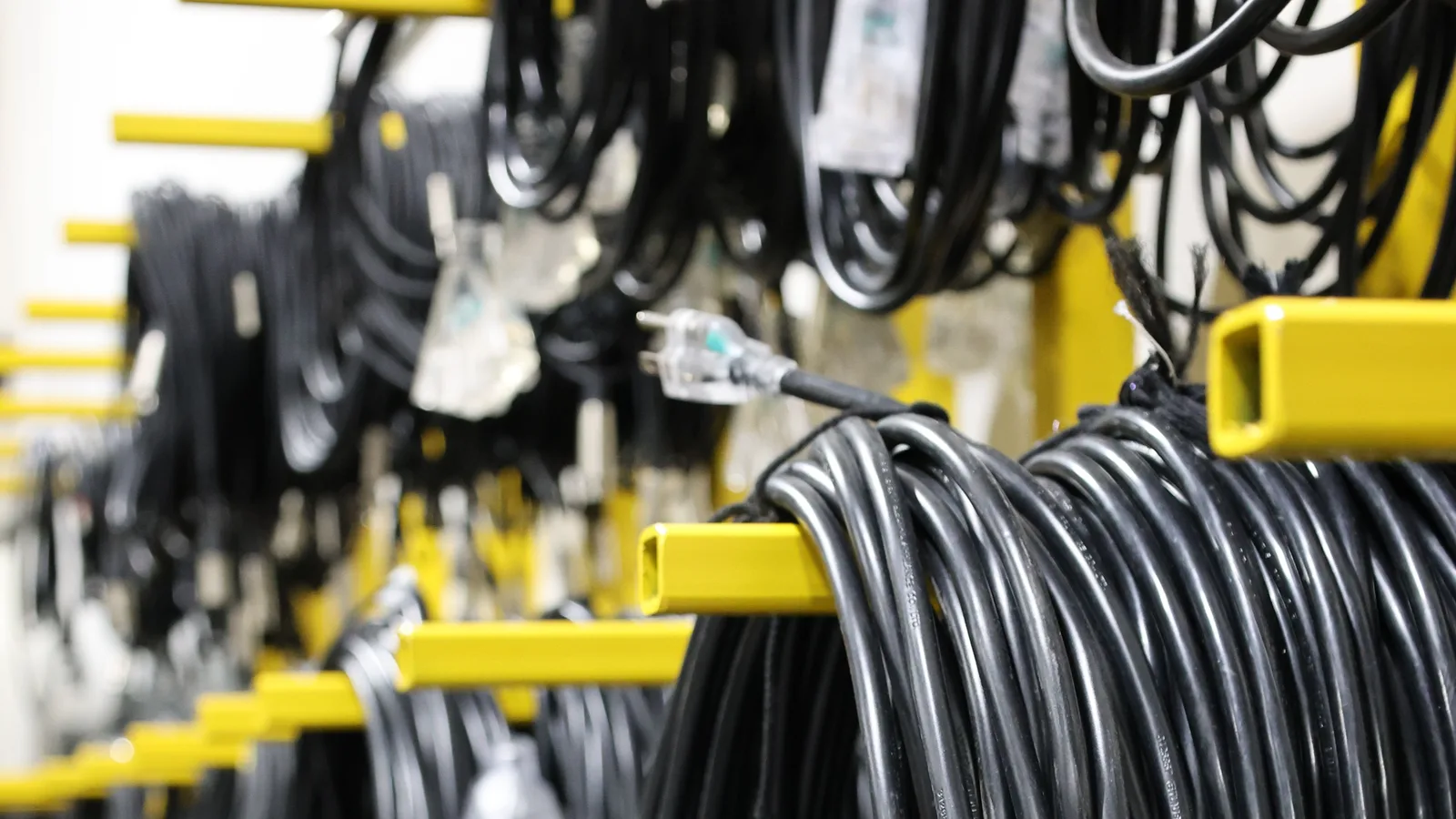Black extension cords hanging in broad loops from wide yellow storage arms