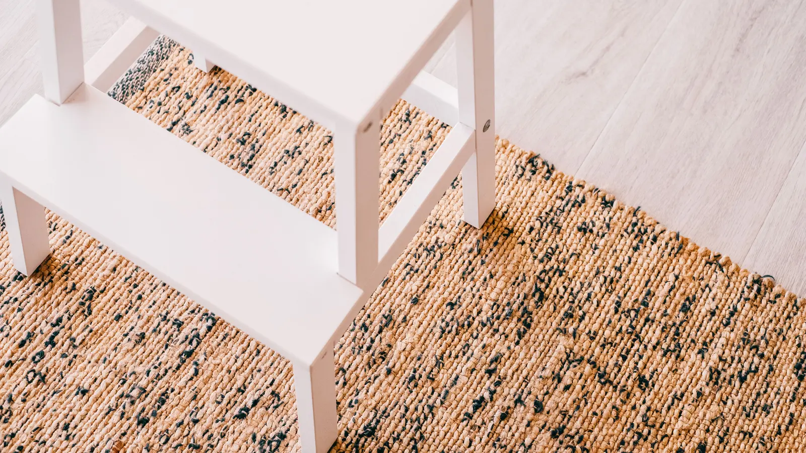 Compact white wooden step stool on a woven rug in a bright home interior